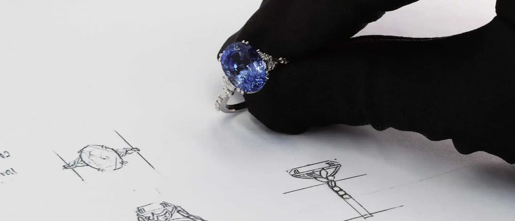 Blue crystal-topped fountain pen sketching jewelry designs on paper.
