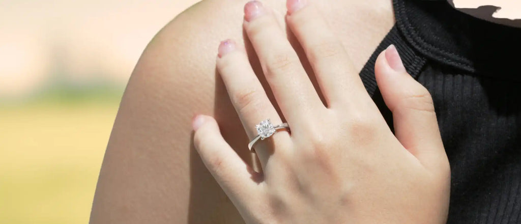 Diamond engagement ring worn on a hand with pink nail polish.